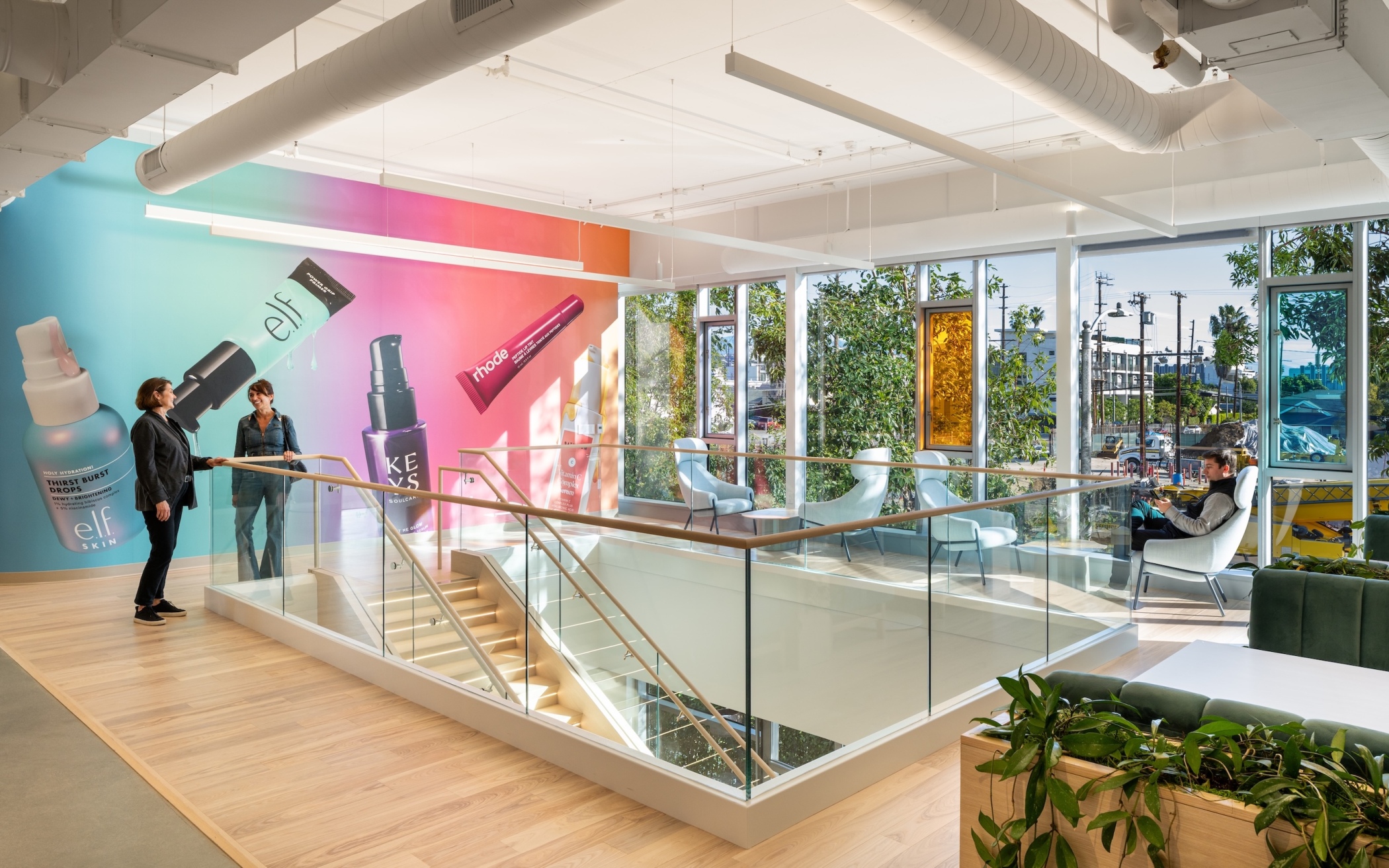 A gallery-like space features a cosmetics mural, glass balustrades, lounge seating and greenery, (Hunter Kerhart Photography)