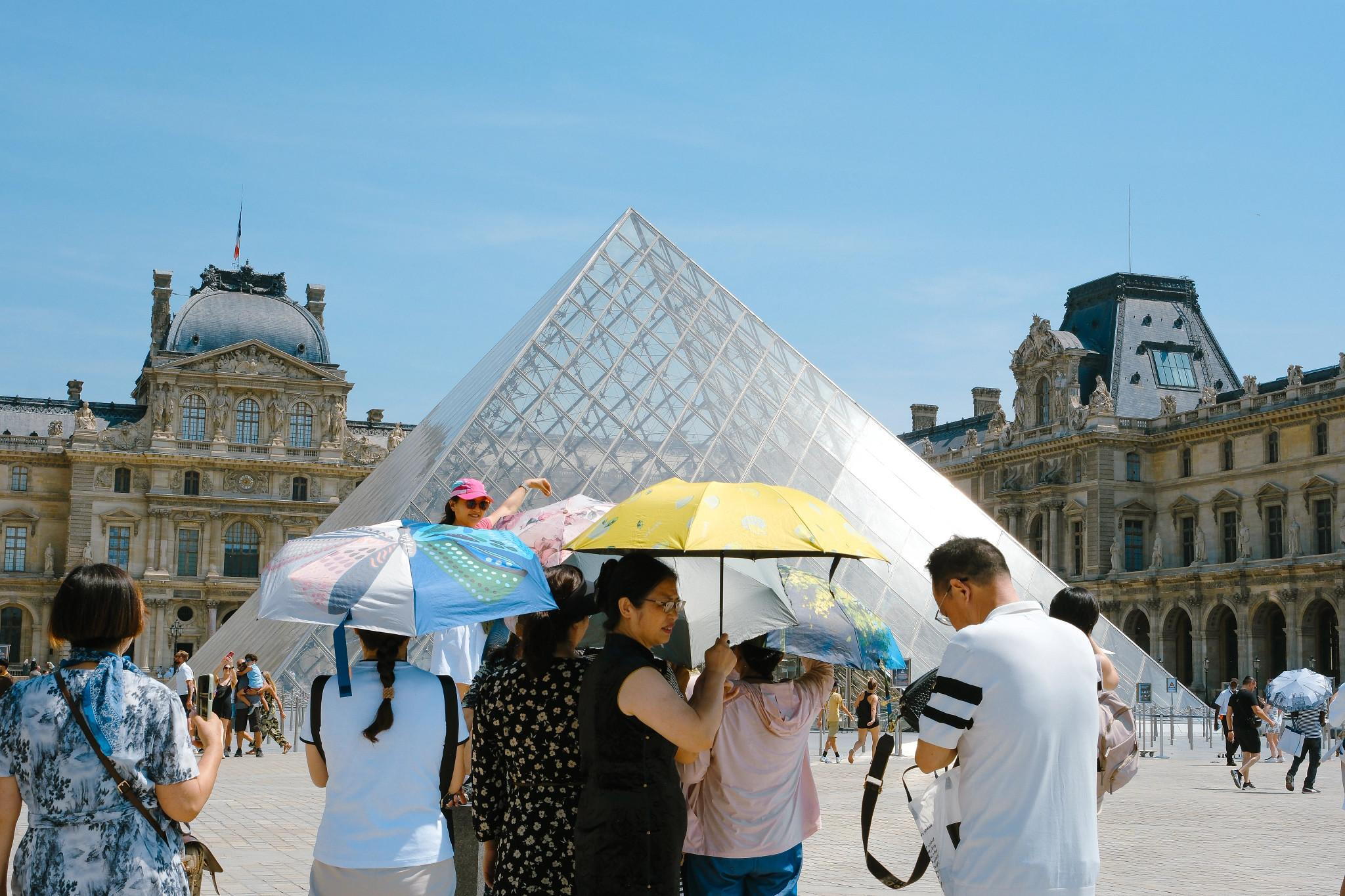 Tourists stand outside the Louvre Museum in Paris, France, on [Month Day, Year]. The museum is adjusting its opening hours due to the prolonged heatwave affecting the French capital. (Photo by Vincent Koebel/NurPhoto via Getty Images) (NurPhoto via Getty Images)