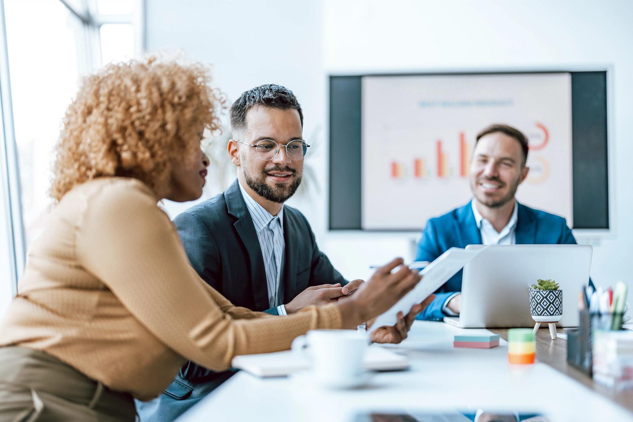 Three professionals are engaged in a business meeting with one man presenting a digital tablet showcasing work-related content (Getty Images)